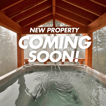 A hot tub with bubbling water sits under a wooden pergola, perfect for relaxation at our Sandpoint vacation rental. New Property Coming Soon! graces the image, while foggy trees in the background hint at a serene, forested escape.